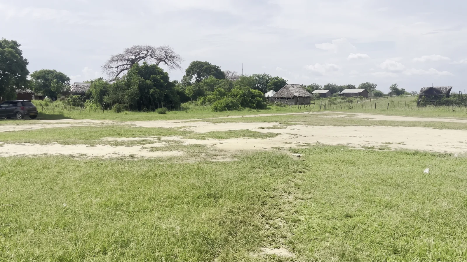Viwanja wazi vilivyozungukwa na miti mikubwa na makazi ya jirani karibu na Mambrui, Kaunti ya Kilifi